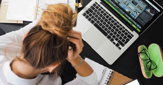 A woman looking at a laptop with her head buried in her hands. She appears very frustrated