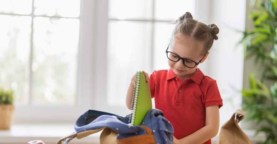 A young girl putting a book into her backpack for school