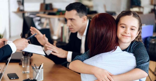A daughter hugging her mother while the father angrily speaks with an attorney