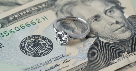 A diamond engagement ring resting on a $20 bill