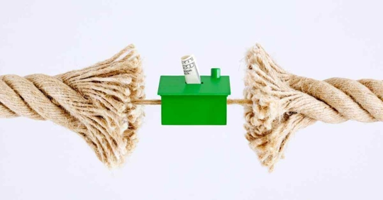 A small toy house being held up by two separate ends of a rope