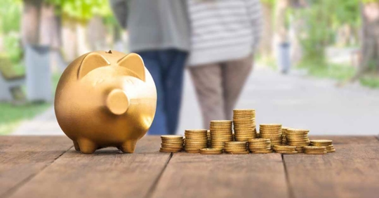 A piggy bank and piles of coins resting on a deck while an older man and woman walk away