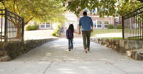 A father and his daughter walking toward a school