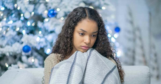 A young woman curled up in a blanket. She appears to be very sad