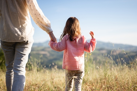 a mother holding daughter's hand in a meadow